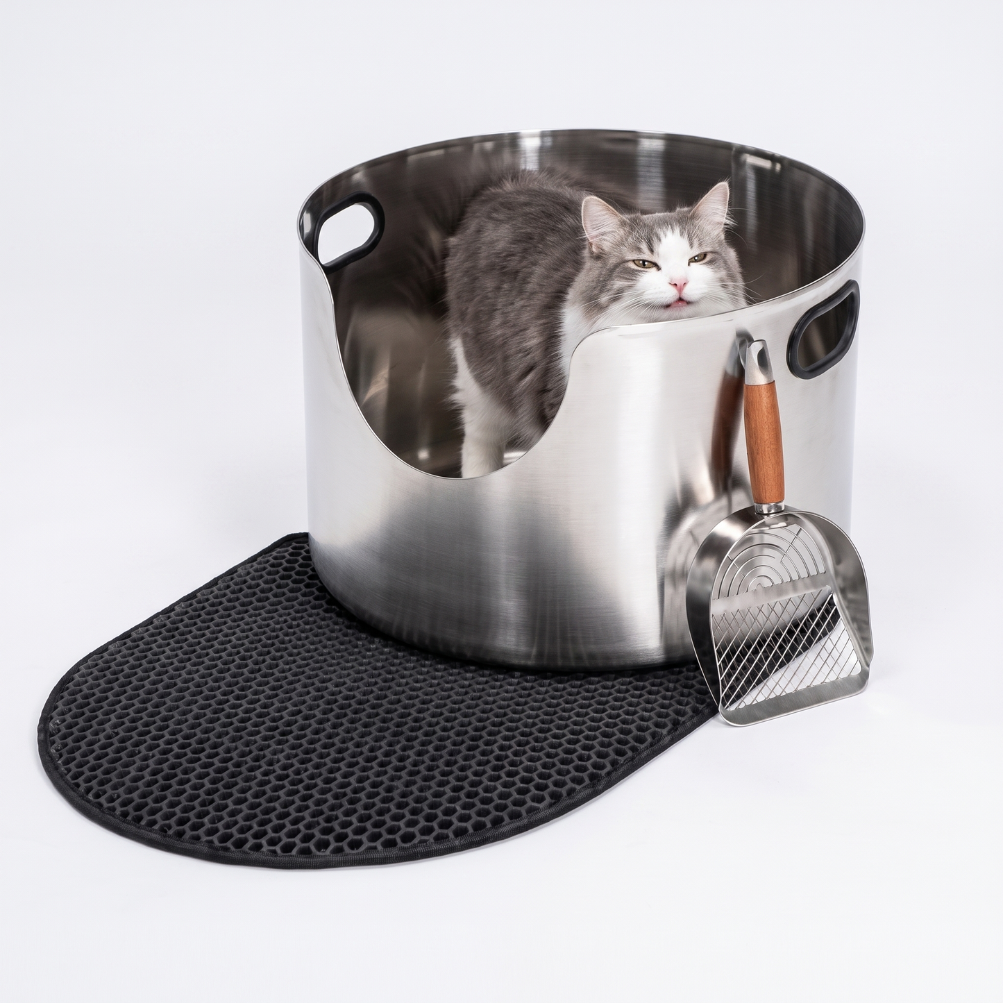 Cat standing inside a round open top stainless steel cat litter box with honeycomb mat and scoop