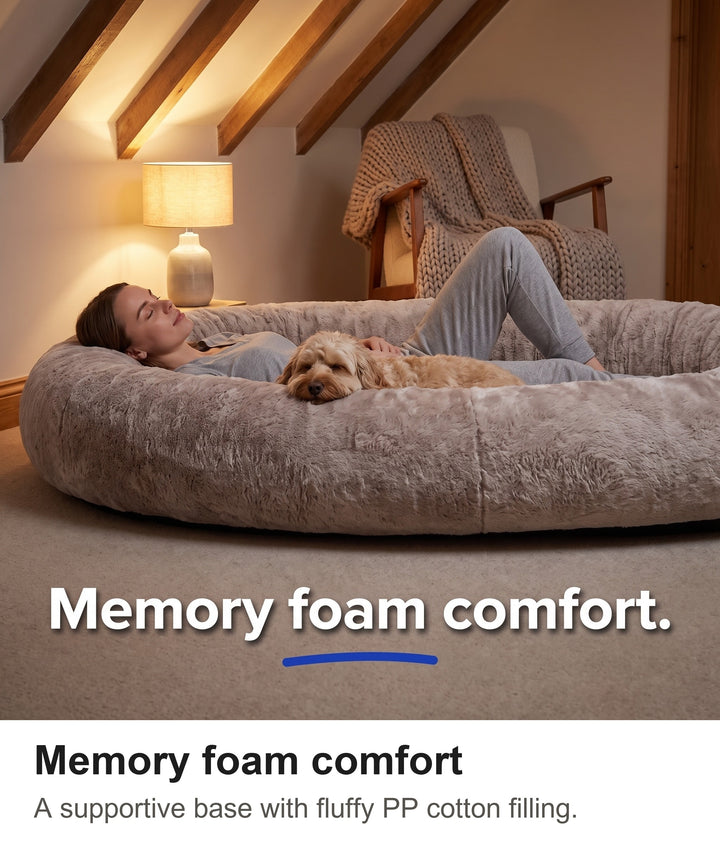 Woman relaxing on her back in the human dog bed with a cockapoo beside her in a cosy bedroom
