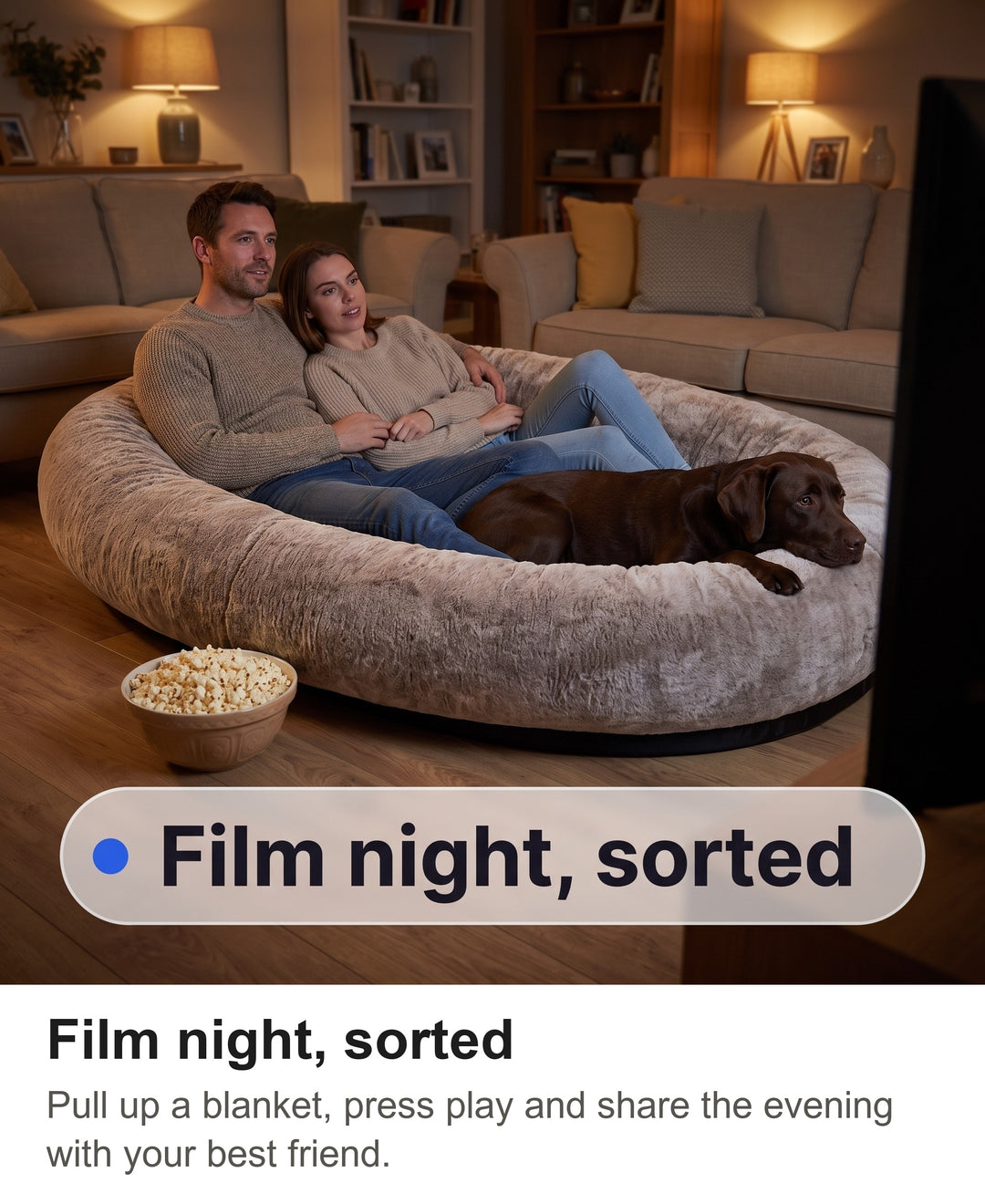 Couple and a Labrador watching a film together in the giant human dog bed