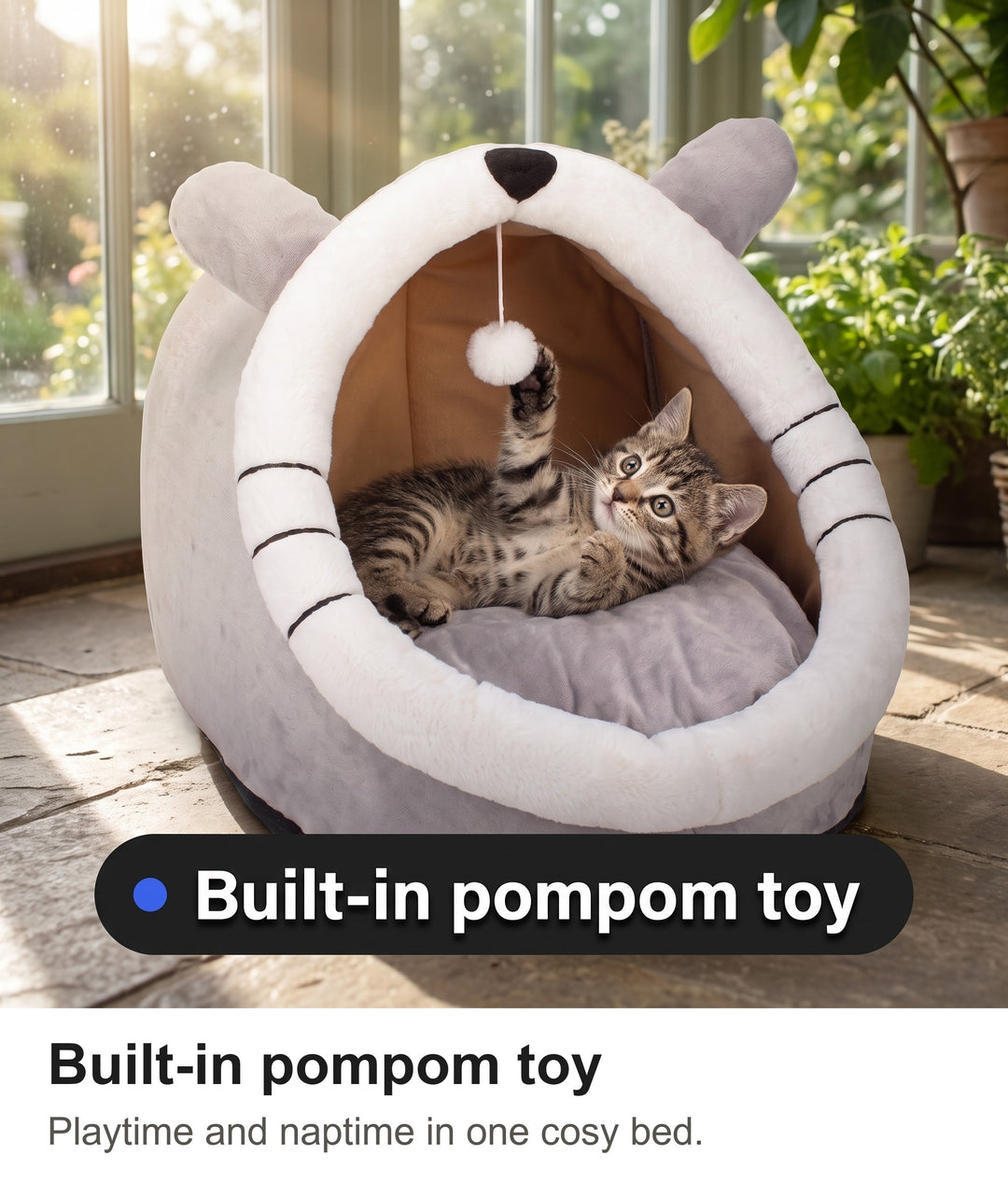 Tabby kitten batting the hanging pompom toy inside the covered cat bed