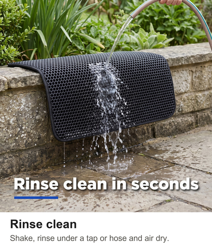 Black cat litter mat being rinsed with a garden hose over a patio wall