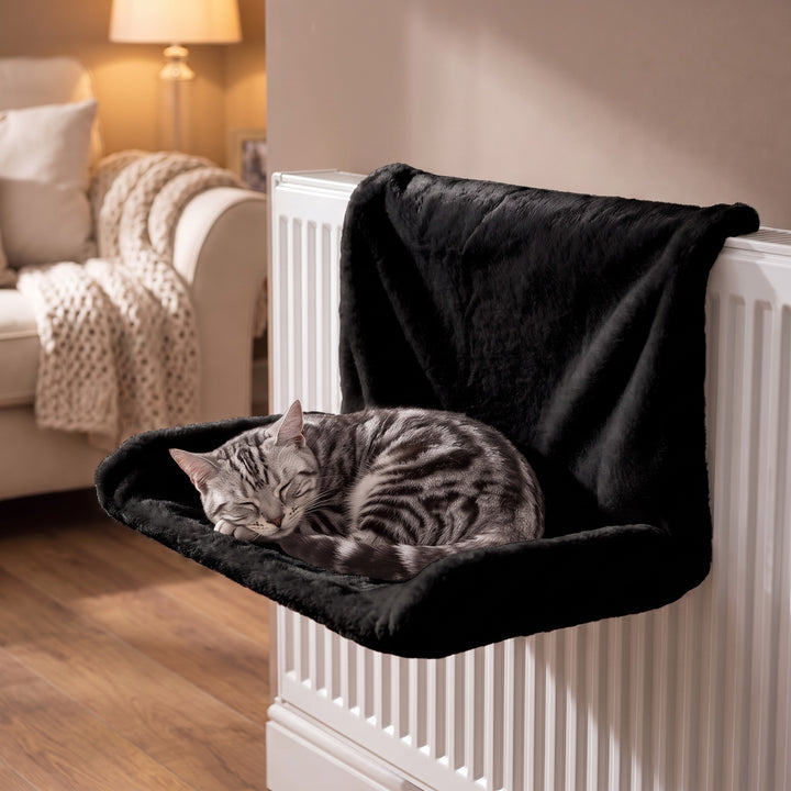 Black plush cat radiator bed hung on a white radiator with a silver tabby cat curled up in it, cosy living room