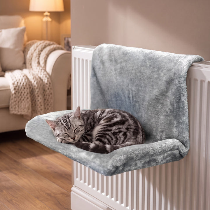 Grey plush cat radiator bed hung on a white radiator with a silver tabby cat curled up in it, cosy living room